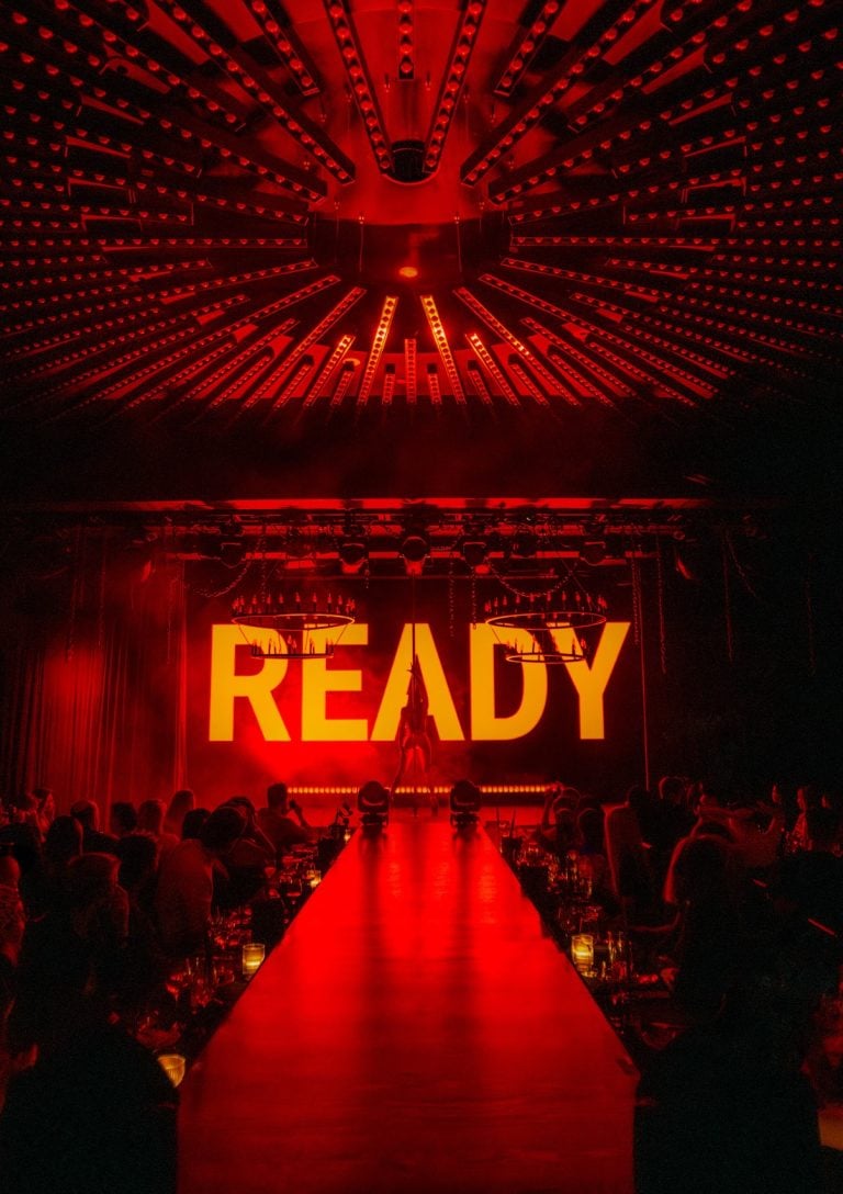A silhouetted figure in front of a red and yellow screen projection with the word "READY"
