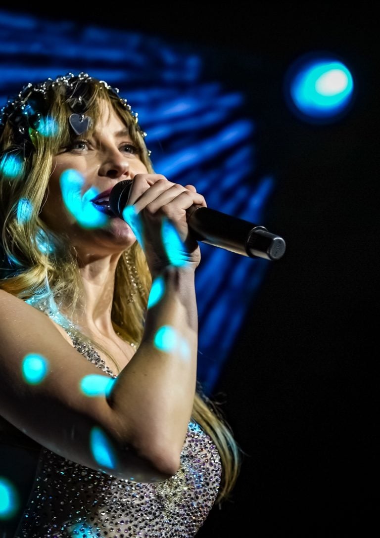 Julianne Hough sings in a microphone with a spotlight shimmering on her