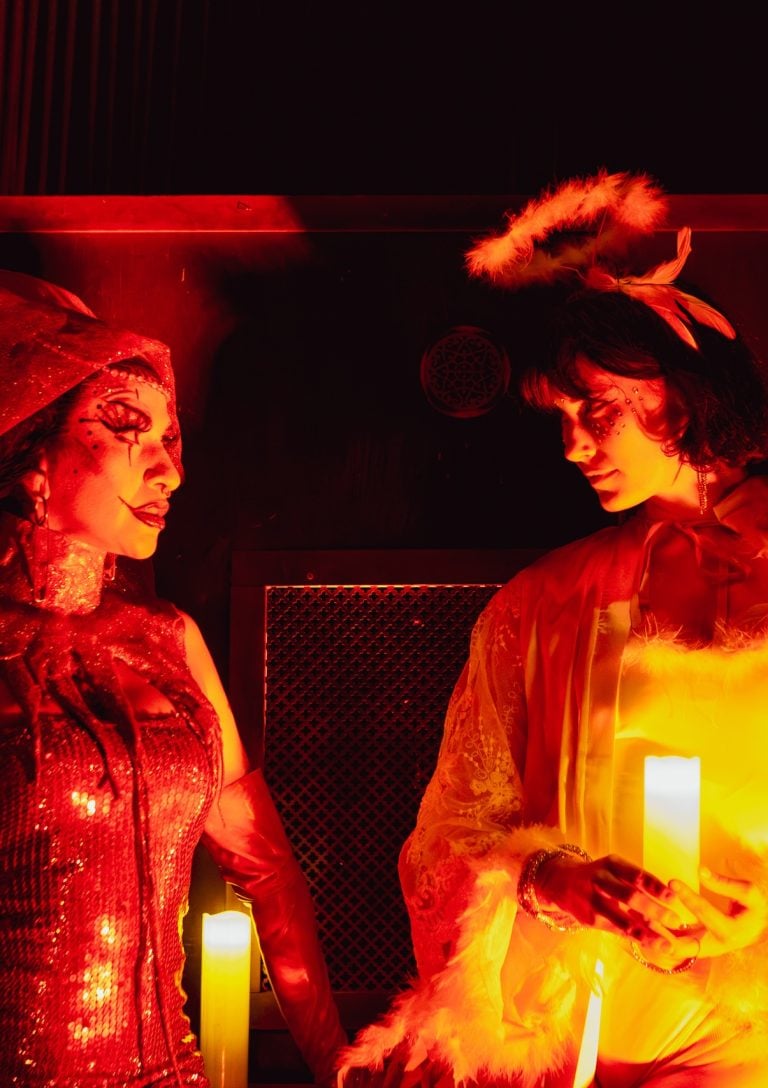 A Paradise Comedy show featuring two characters holding candles, dressed as an angel and devil