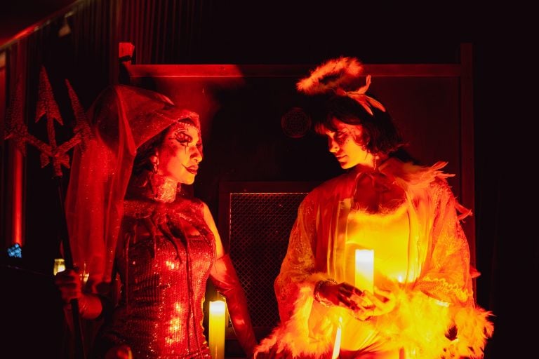 A Paradise Comedy show featuring two characters holding candles, dressed as an angel and devil