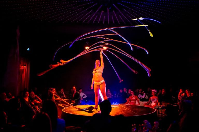 A performers in Moonrise holds a a large, spiky wood structure above their head