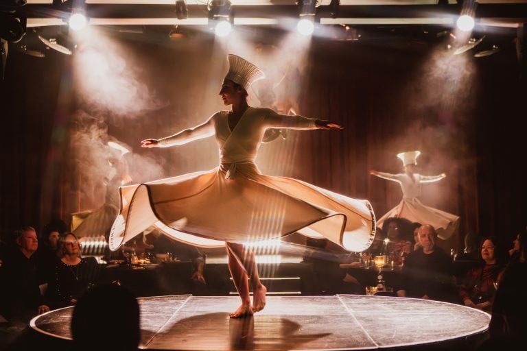 A woman with a white dress and tall round had spins on stage at the Paradise Club