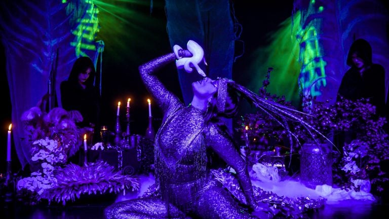 A performer in Moonrise holds a snake close to her face