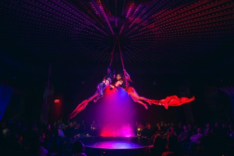 Two intertwined aerialists hanging from scarves embrace