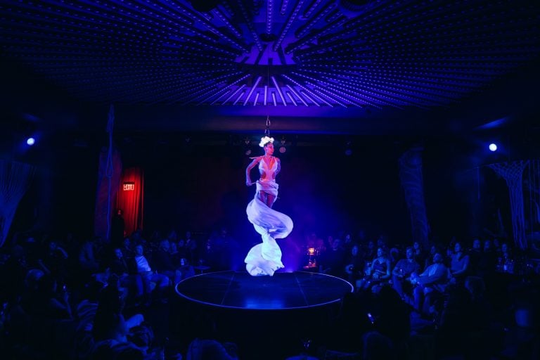 A performer in a long white dress hangs from a harness