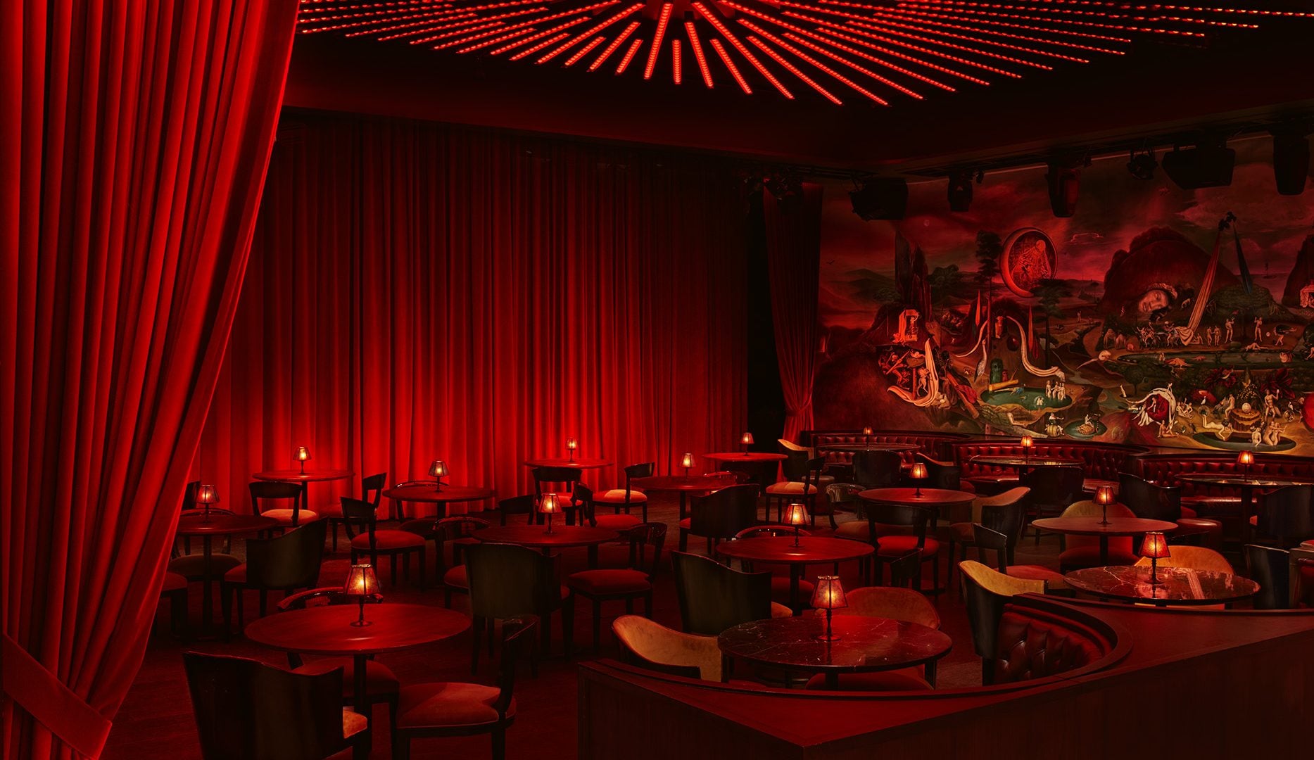 A sitting area at the Paradise Club, with circular booths and cabaret tables, with red curtain walls and a large mural