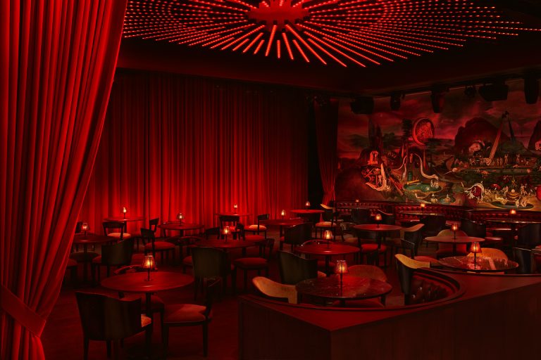 A sitting area at the Paradise Club, with circular booths and cabaret tables, with red curtain walls and a large mural